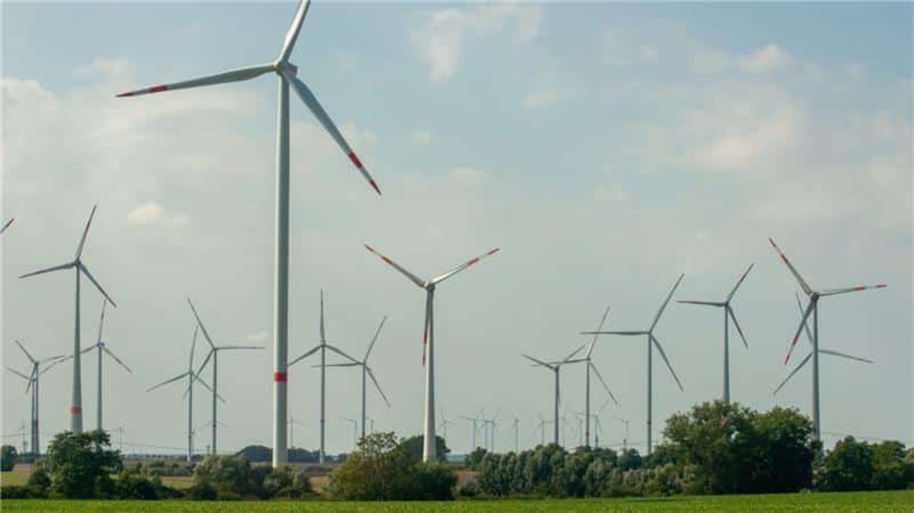 Wind turbines standing across a green field under a partly cloudy sky.