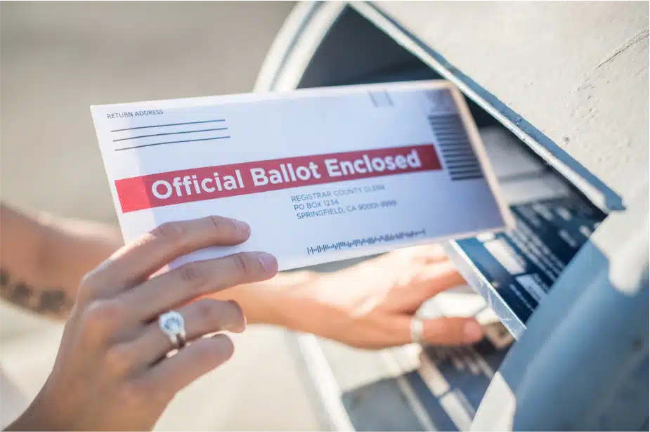 a hand dropping off a voting ballot in the mail box